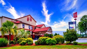 Ein Red Roof Inn mit rotem Dach und beigen Wänden, umgeben von gepflegter Bepflanzung und Palmen.