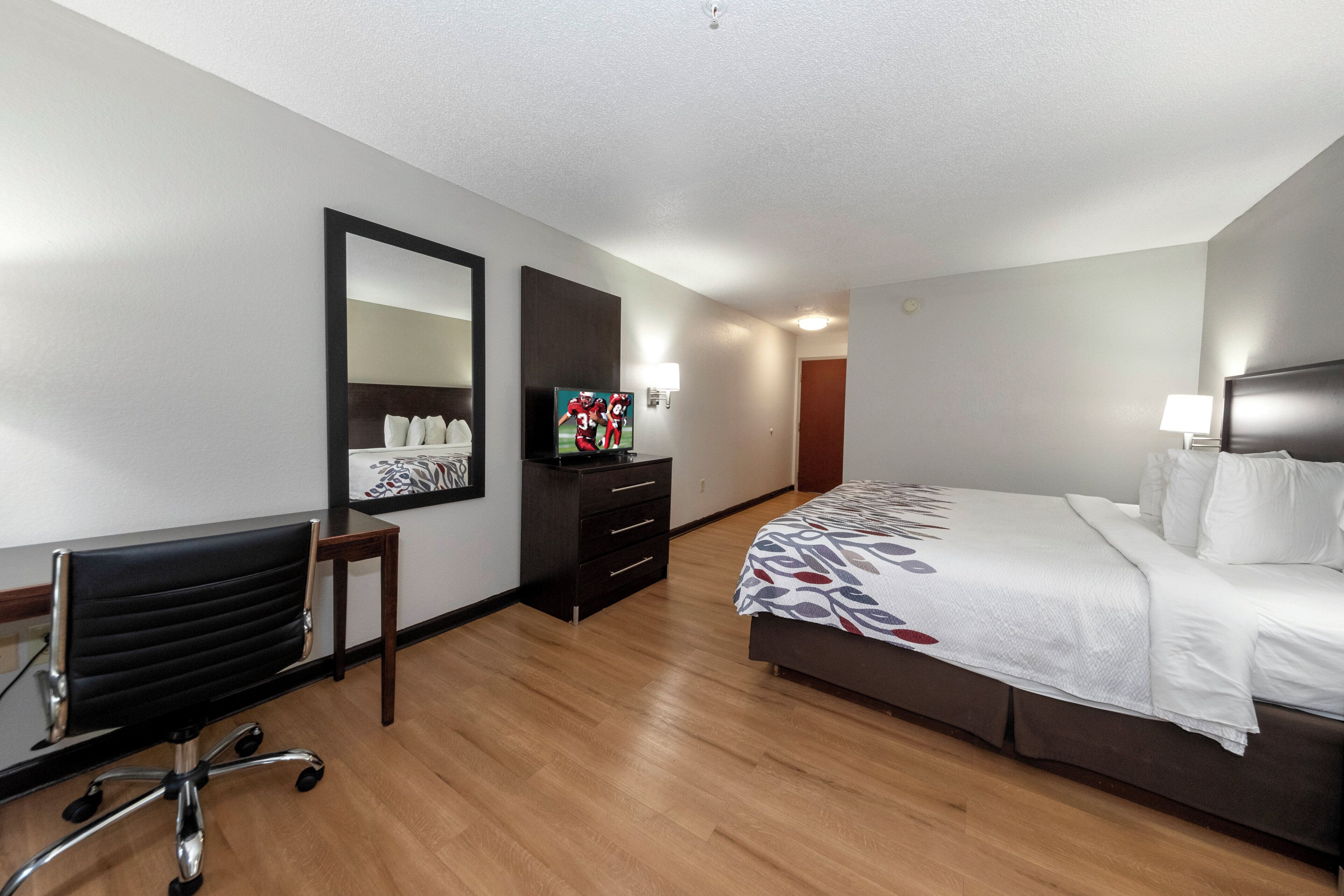 A hotel room with a bed, a desk, a chair, a dresser, a mirror, and a television.