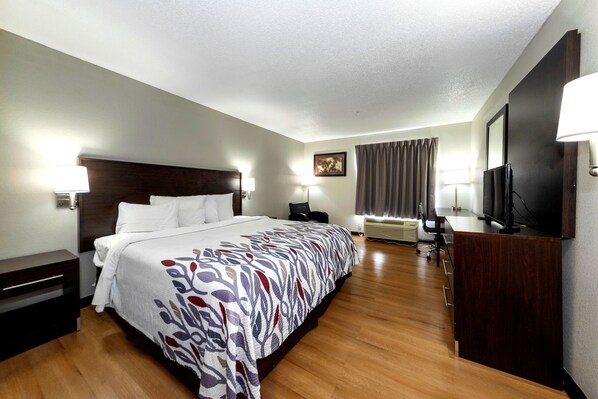 A hotel room with a large bed, bedside tables, a desk with a chair, a television, and a window with curtains. - Red Roof Inn Atlanta Southeast - Stockbridge (Stockbridge)