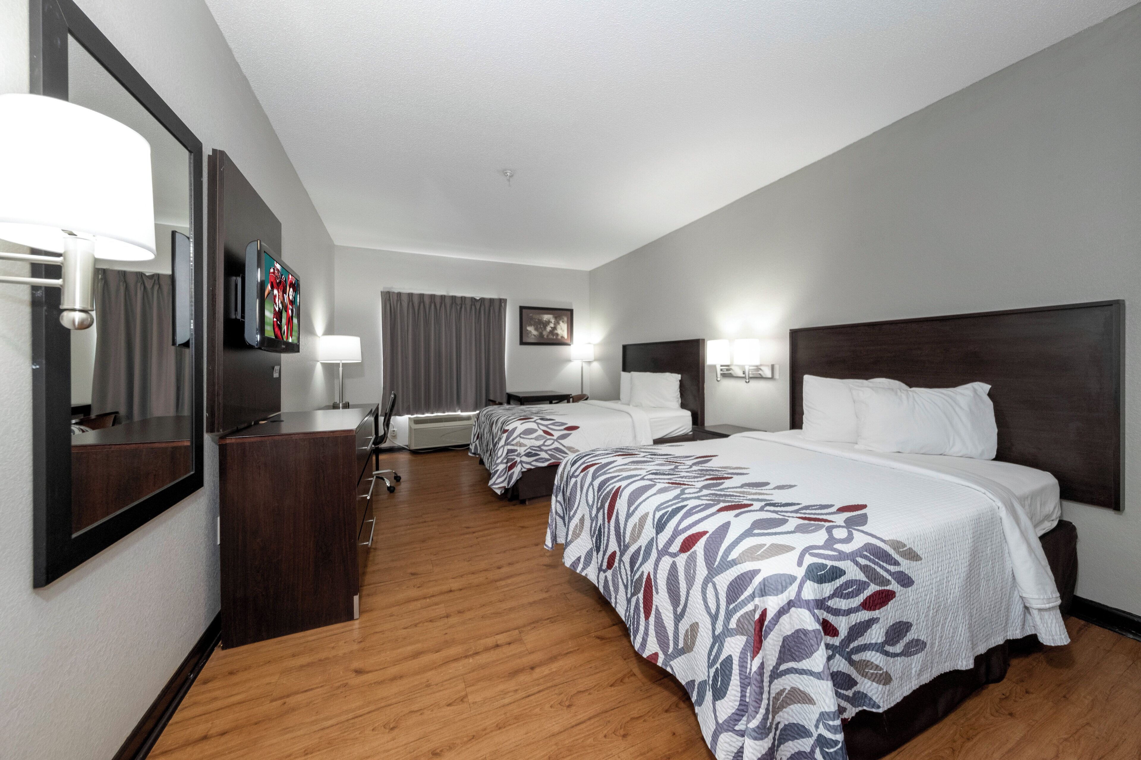 Een hotelkamer met een groot bed, een bureau, een stoel, een aan de muur bevestigde televisie en een raam met gordijnen.