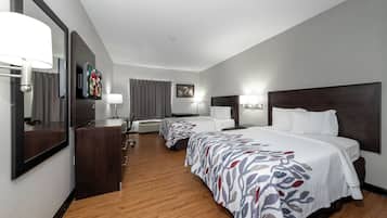 A hotel room with a large bed, a desk, a chair, a TV mounted on the wall, and a window with curtains.
