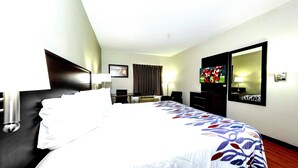 A hotel room with a bed, a desk, a chair, a TV, and a mirror. - Red Roof Inn Atlanta Southeast - Stockbridge (Stockbridge)