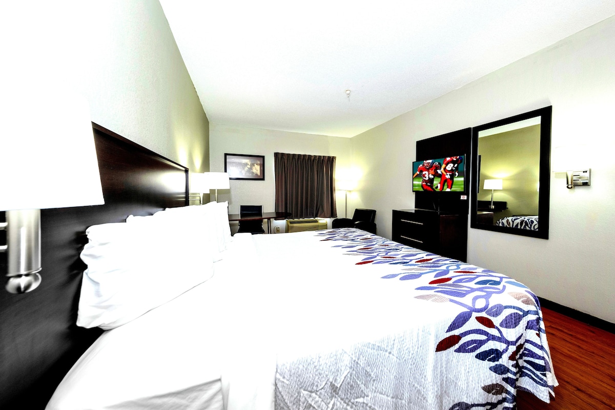 A hotel room with a bed, a desk, a chair, a TV, and a mirror.