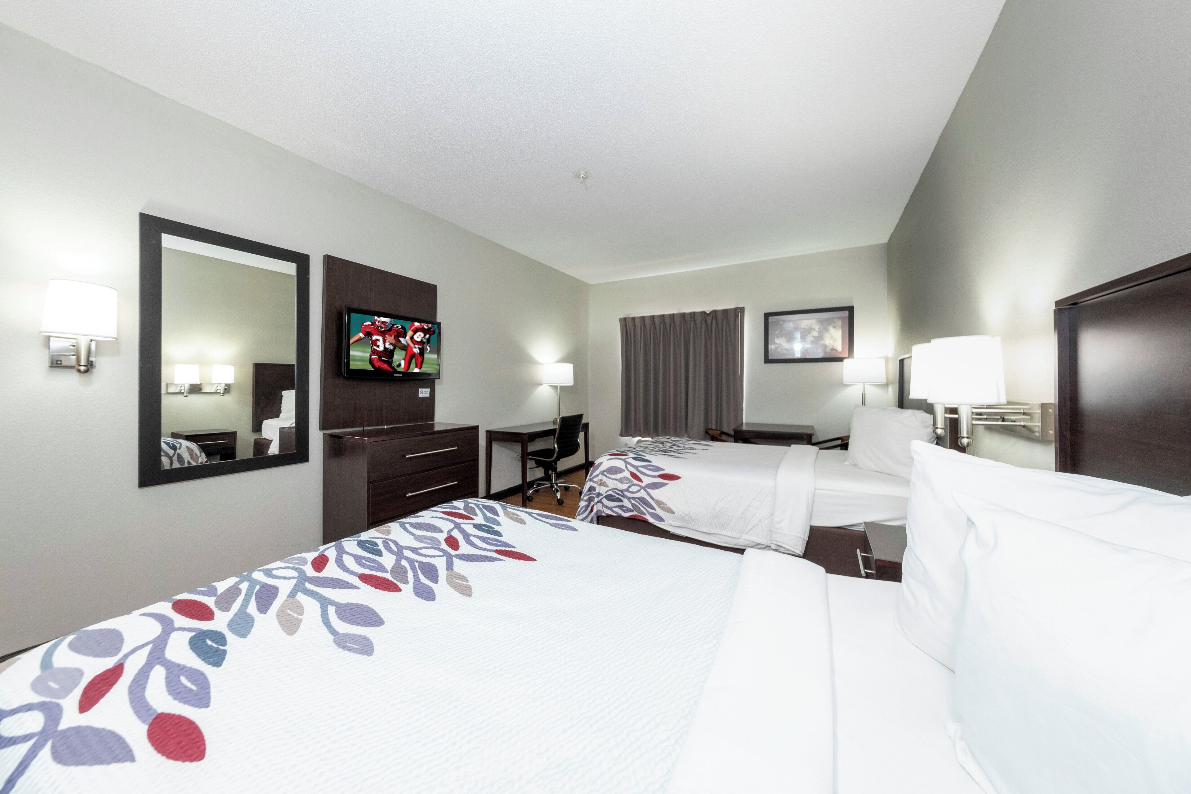A hotel room with two beds, a desk, a chair, a television, and a bathroom.