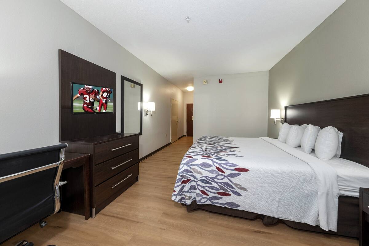 Une chambre d’hôtel avec un grand lit, une commode, un téléviseur fixé au mur et une porte donnant sur une autre pièce.