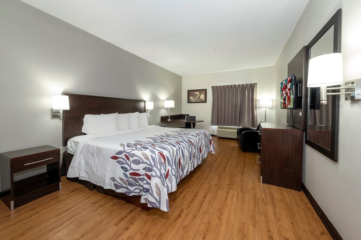 A hotel room with a large bed, bedside tables, a desk, a television, and a mirror.