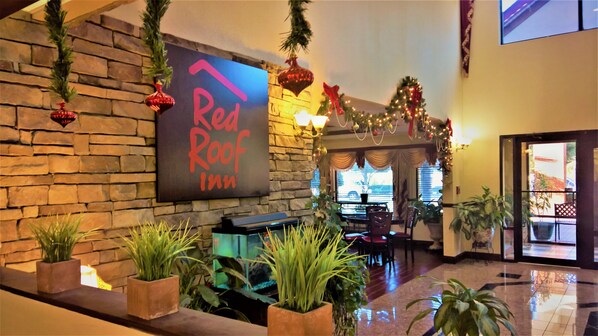 A Red Roof Inn lobby with a stone wall, a sign, potted plants, a reception desk, and a Christmas tree. - Red Roof Inn Atlanta Southeast - Stockbridge (Stockbridge)