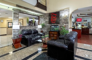 A hotel lobby with a black leather sofa, a fish tank, and a Red Roof Inn sign. - Red Roof Inn Atlanta Southeast - Stockbridge (Stockbridge)