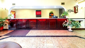 A reception area with a marble floor, wooden reception desk, and potted plants. - Red Roof Inn Atlanta Southeast - Stockbridge (Stockbridge)