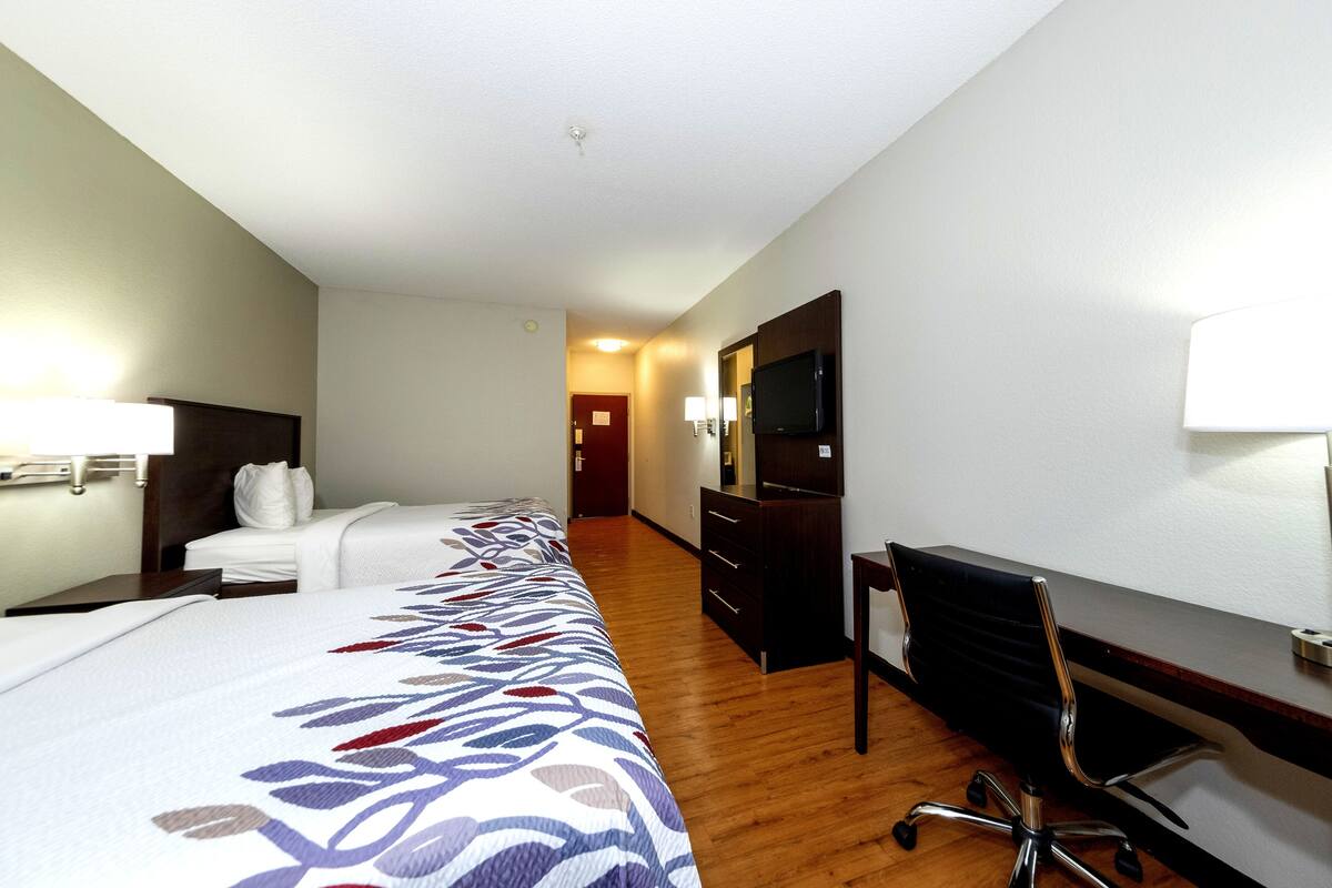Une chambre d’hôtel avec un grand lit, un bureau avec une chaise, une télévision et une commode.