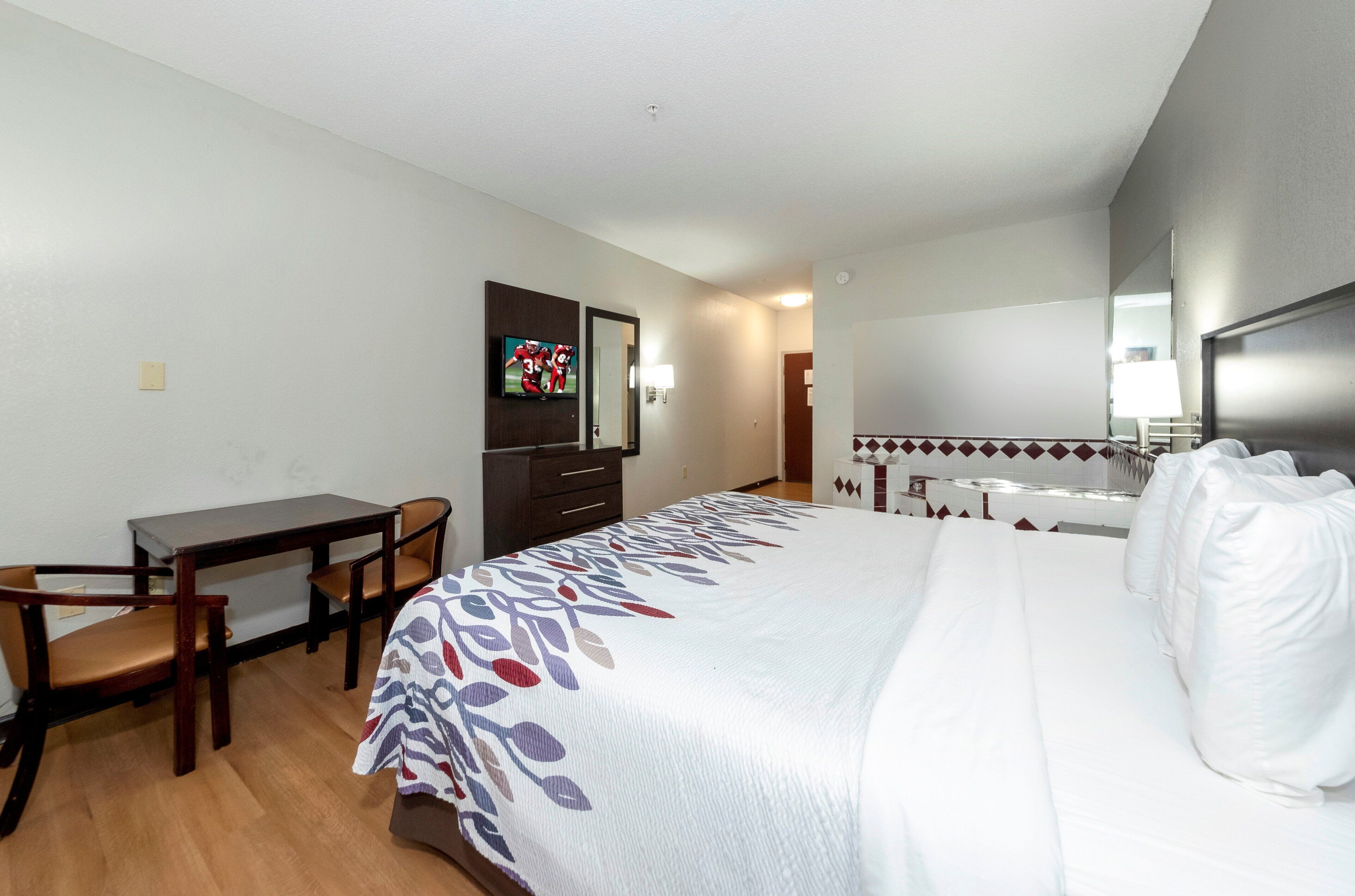 A hotel room with a bed, a desk, a chair, a television, and a mirror.