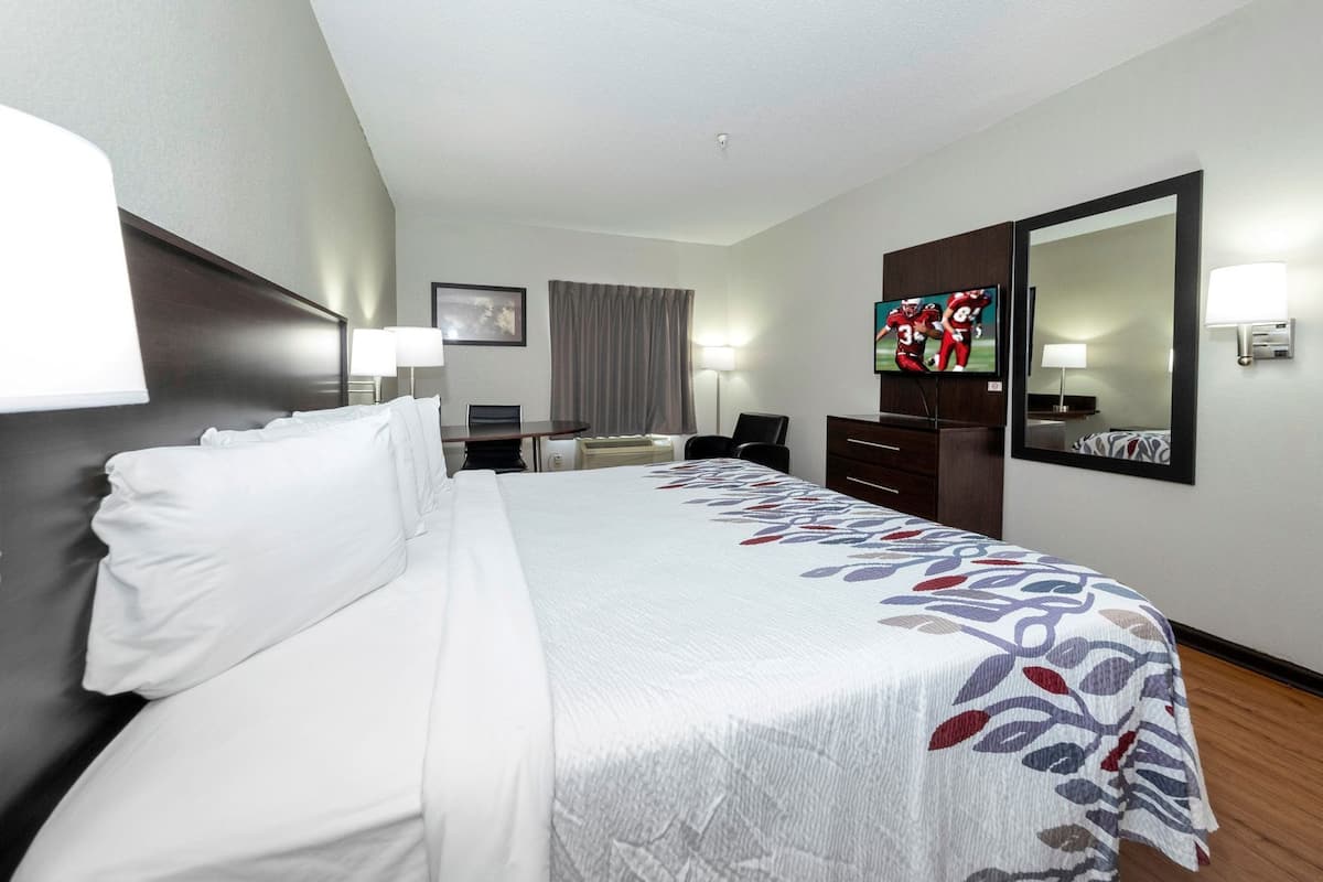 A hotel room with a large bed, a desk, a chair, a television, and a mirror.