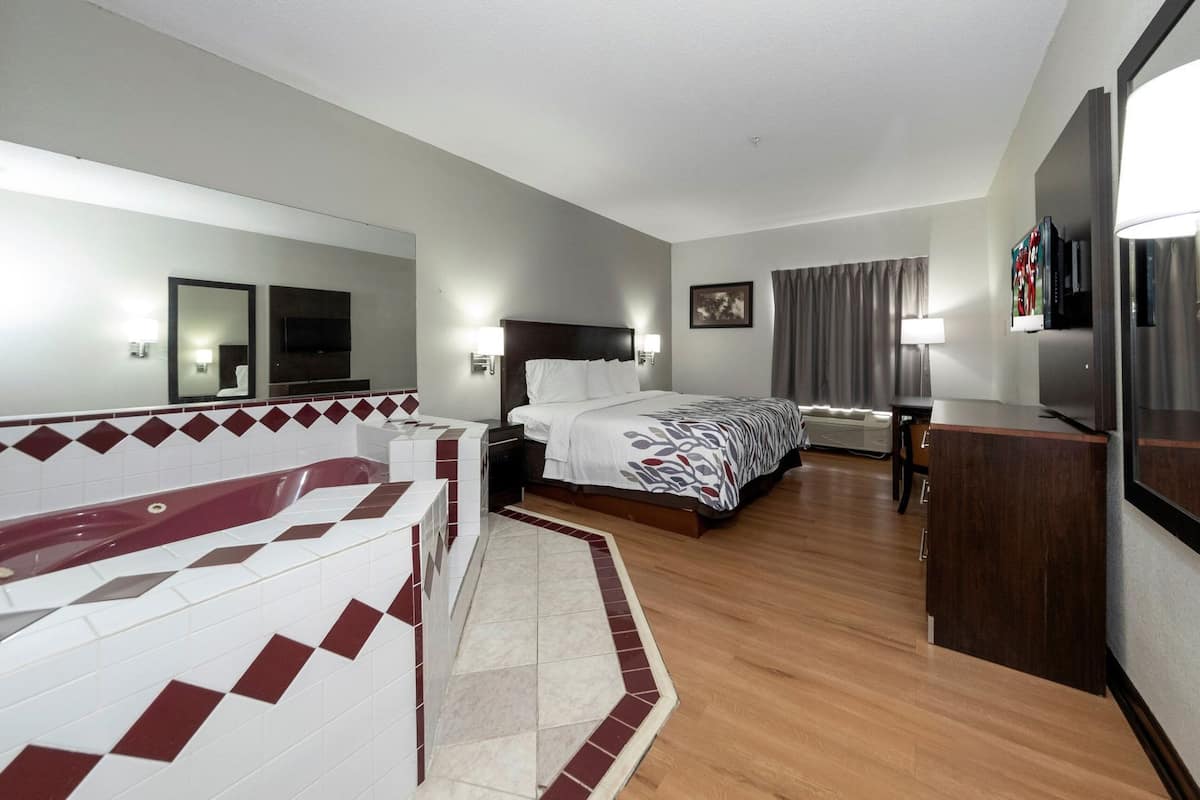 A hotel room with a bed, a desk, a TV, a bathroom with a tub, and a shower.