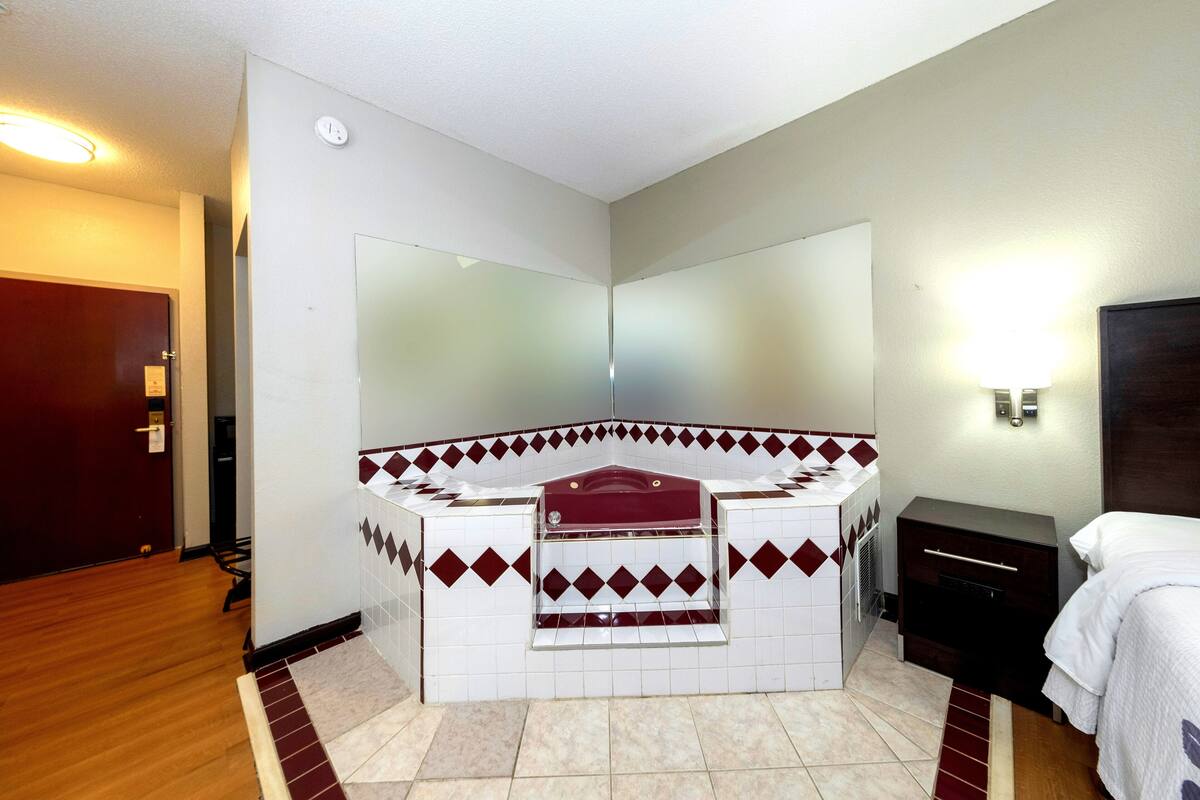 Une salle de bain d’hôtel avec un lavabo d’angle, un miroir, une commode et un lit.