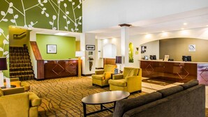 A hotel lobby with a reception desk, seating area, and a staircase.