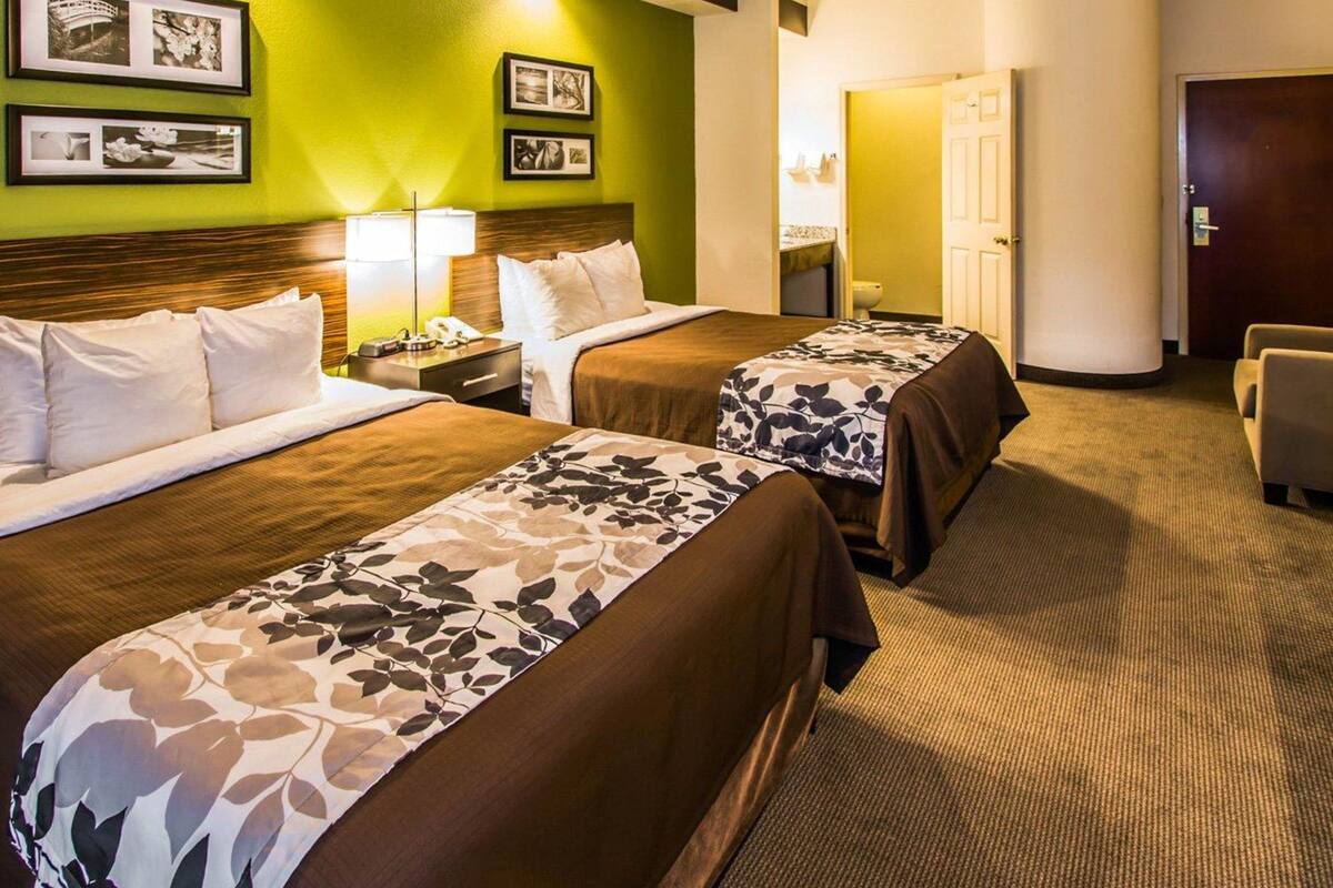 A hotel room with two beds, a wooden headboard, a green accent wall, and framed pictures.