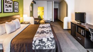 A hotel room with a bed, a desk, a television, and a bathroom visible through an archway.