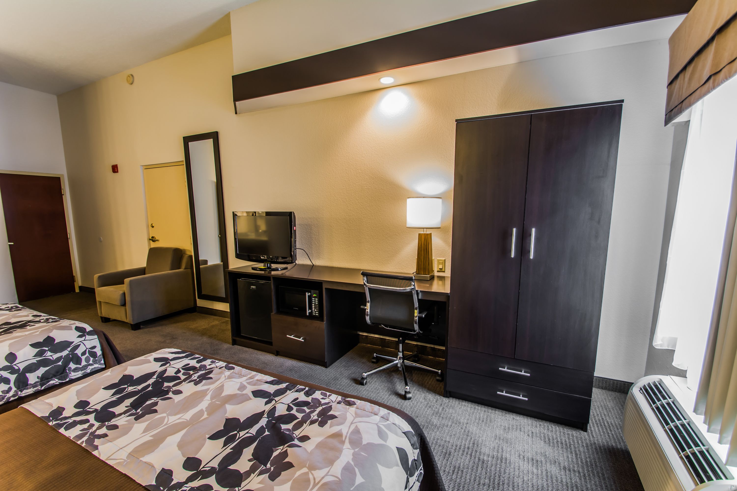 A hotel room with two beds, a desk with a computer, a TV, a wardrobe, and a heater.