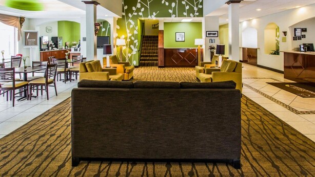 A hotel lobby with a central seating area, a reception desk, and a staircase leading to an upper floor.