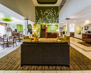 Un vestíbulo de hotel con una zona de estar central, una recepción y una escalera que lleva a un piso superior.