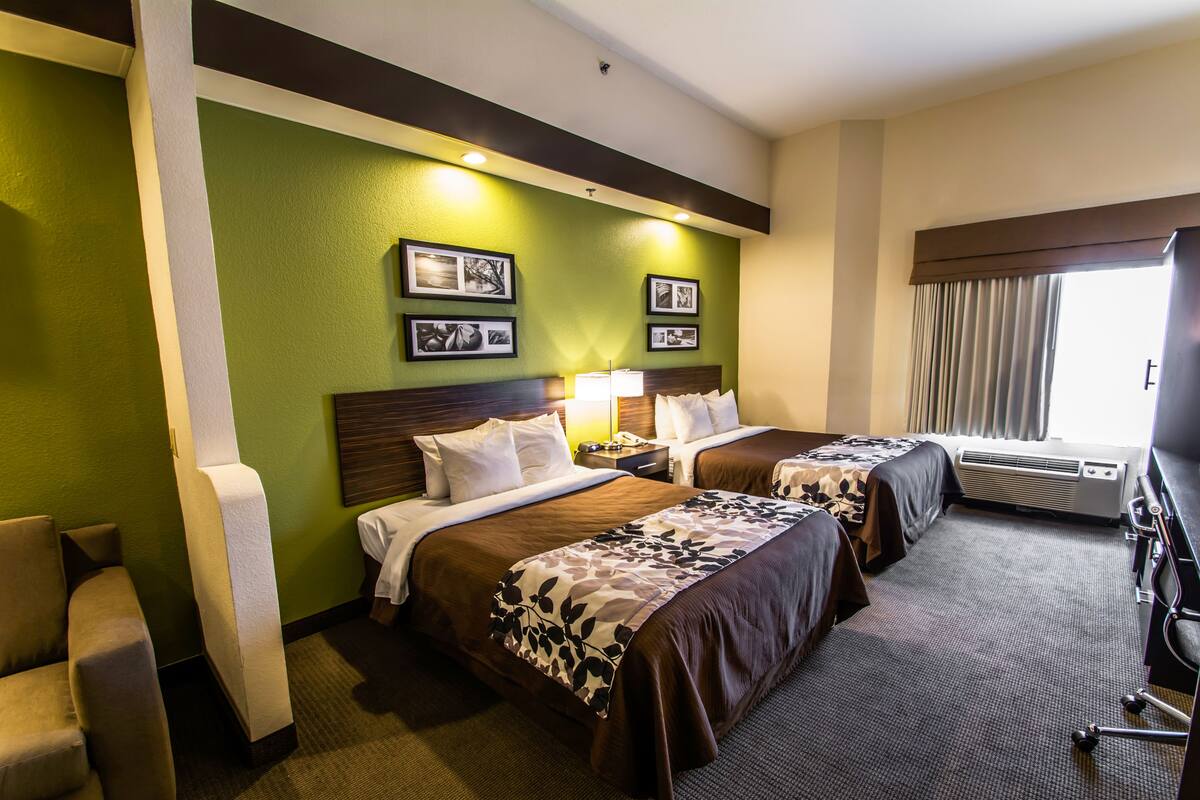 A hotel room with two beds, a desk, a chair, and a window with curtains.