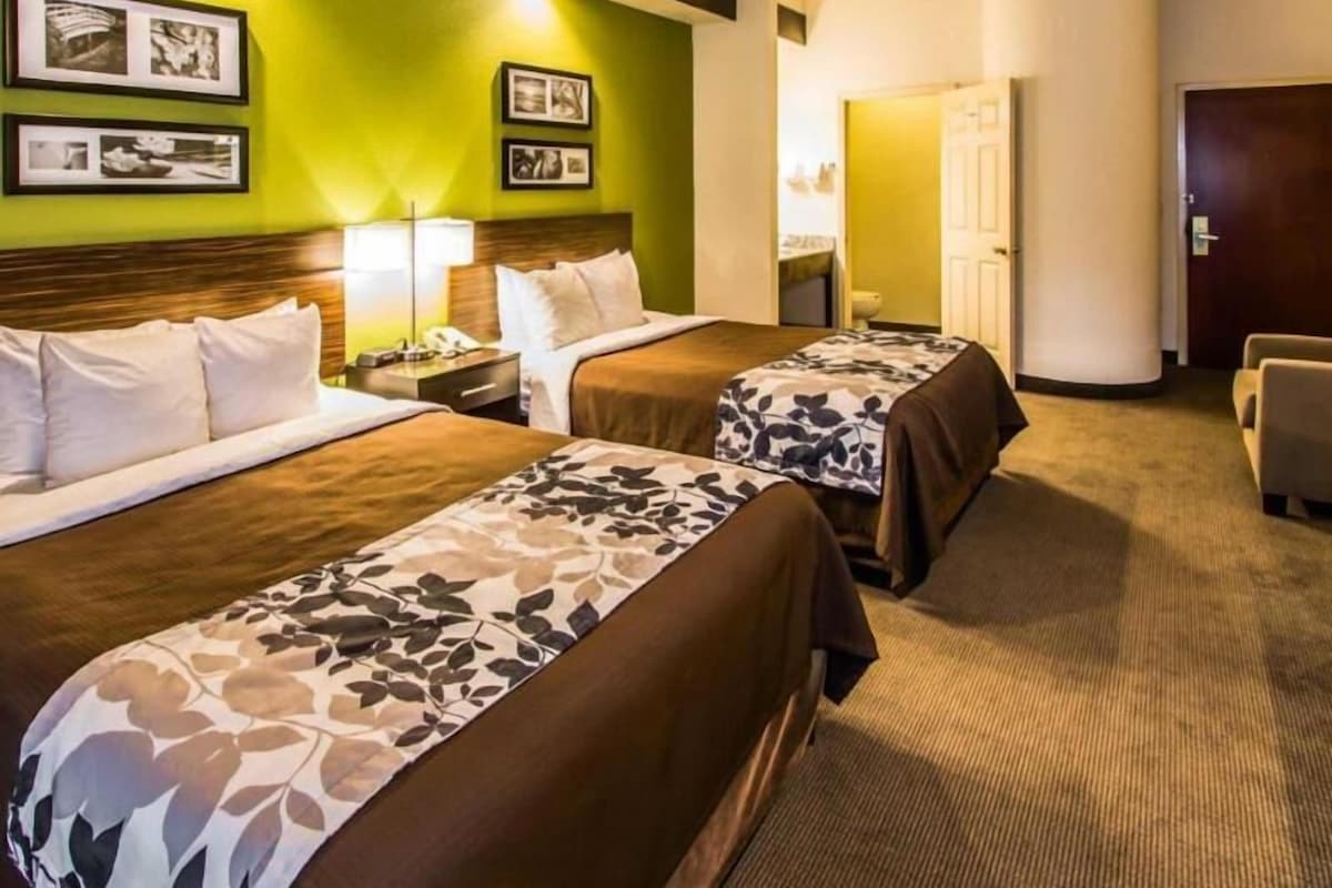 A hotel room with two beds, a desk, a chair, and a door.