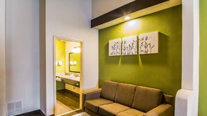 A hotel room with a sofa, a small table, and a green accent wall with artwork.