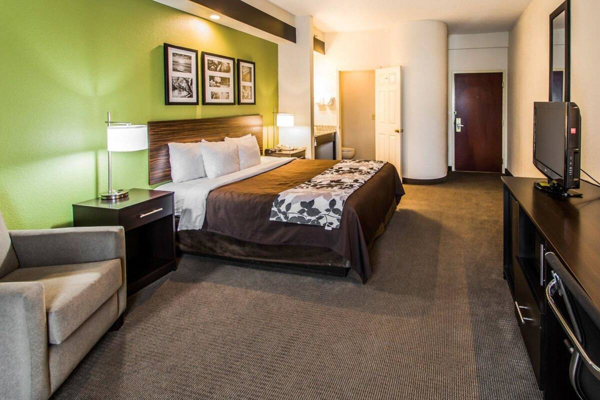 A hotel room with a bed, a desk, a chair, a television, and a wall with framed pictures.