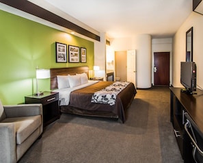 A hotel room with a bed, a desk, a chair, a television, and a wall with framed pictures.