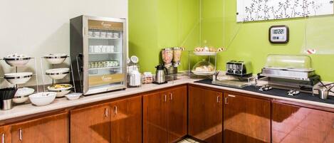 A breakfast area with a coffee machine, a display case with food items, and a clock on the wall.