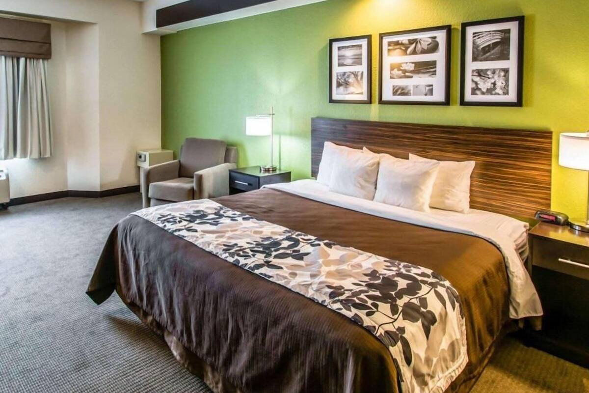 A hotel room with a large bed, a chair, a nightstand, a lamp, and three framed pictures on the wall.