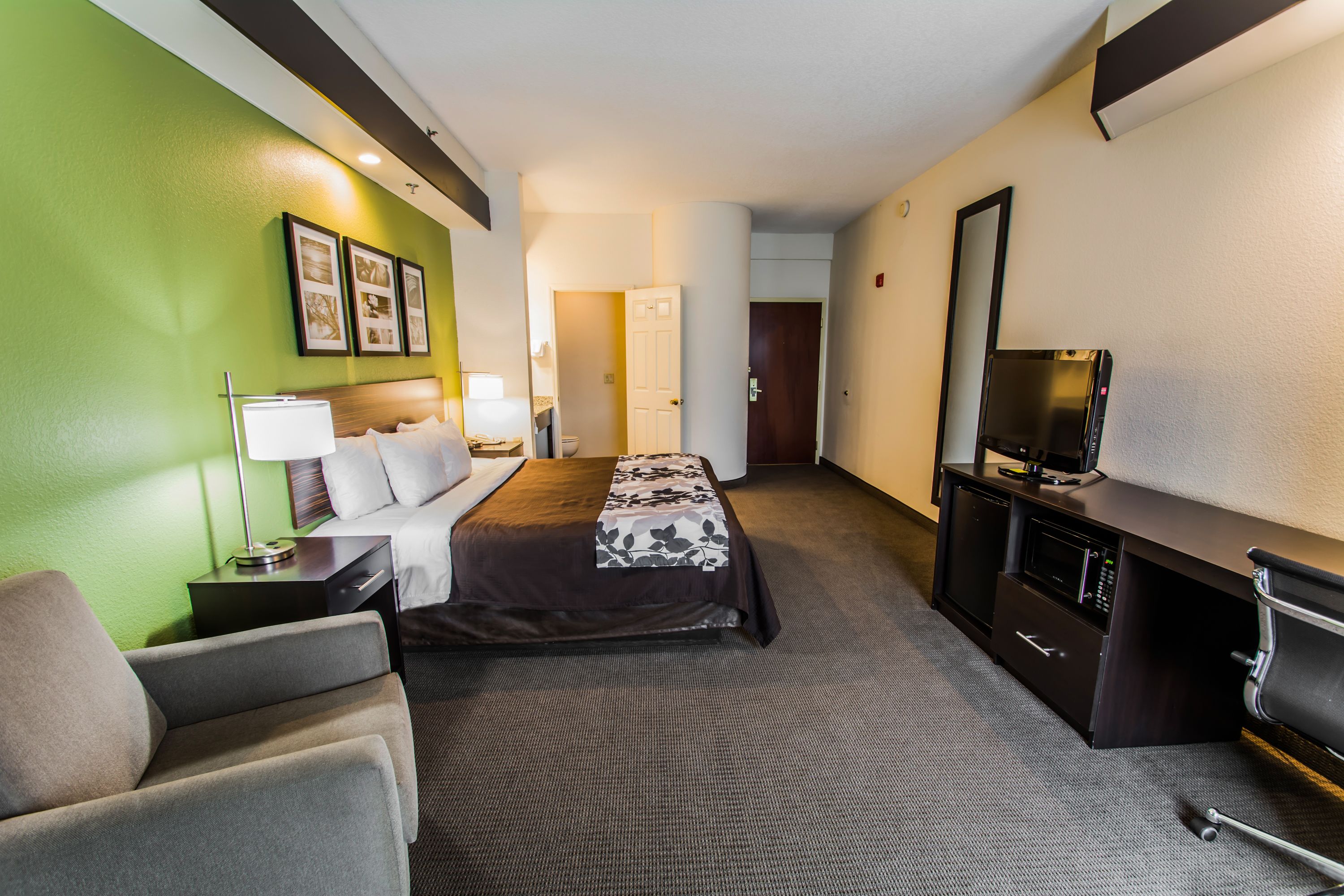 A hotel room with a bed, a desk with a television, a chair, and a lamp.