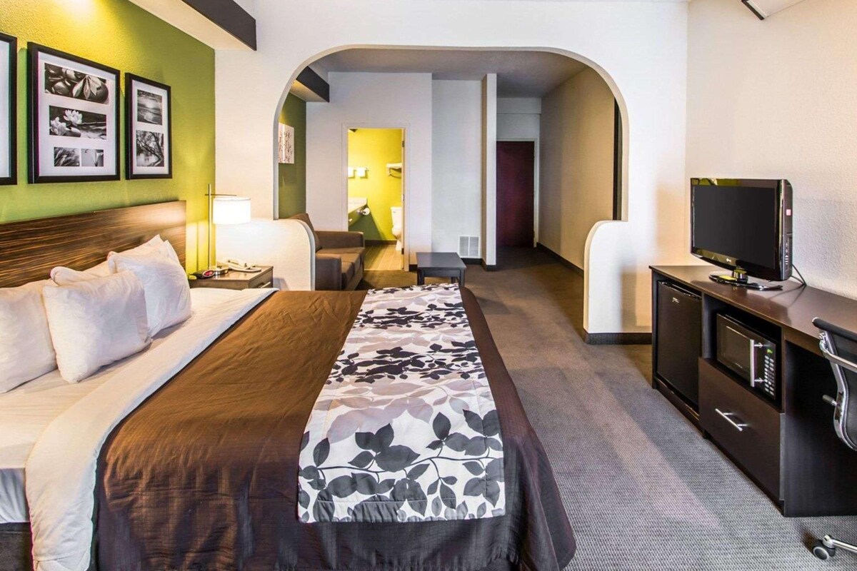 A hotel room with a bed, a desk, a television, and a bathroom visible through an archway.