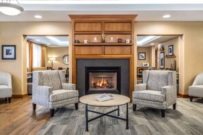 A hotel lobby with a fireplace, two armchairs, a coffee table, and a wooden shelf above the fireplace. - Hampton Inn Waterville (Waterville)