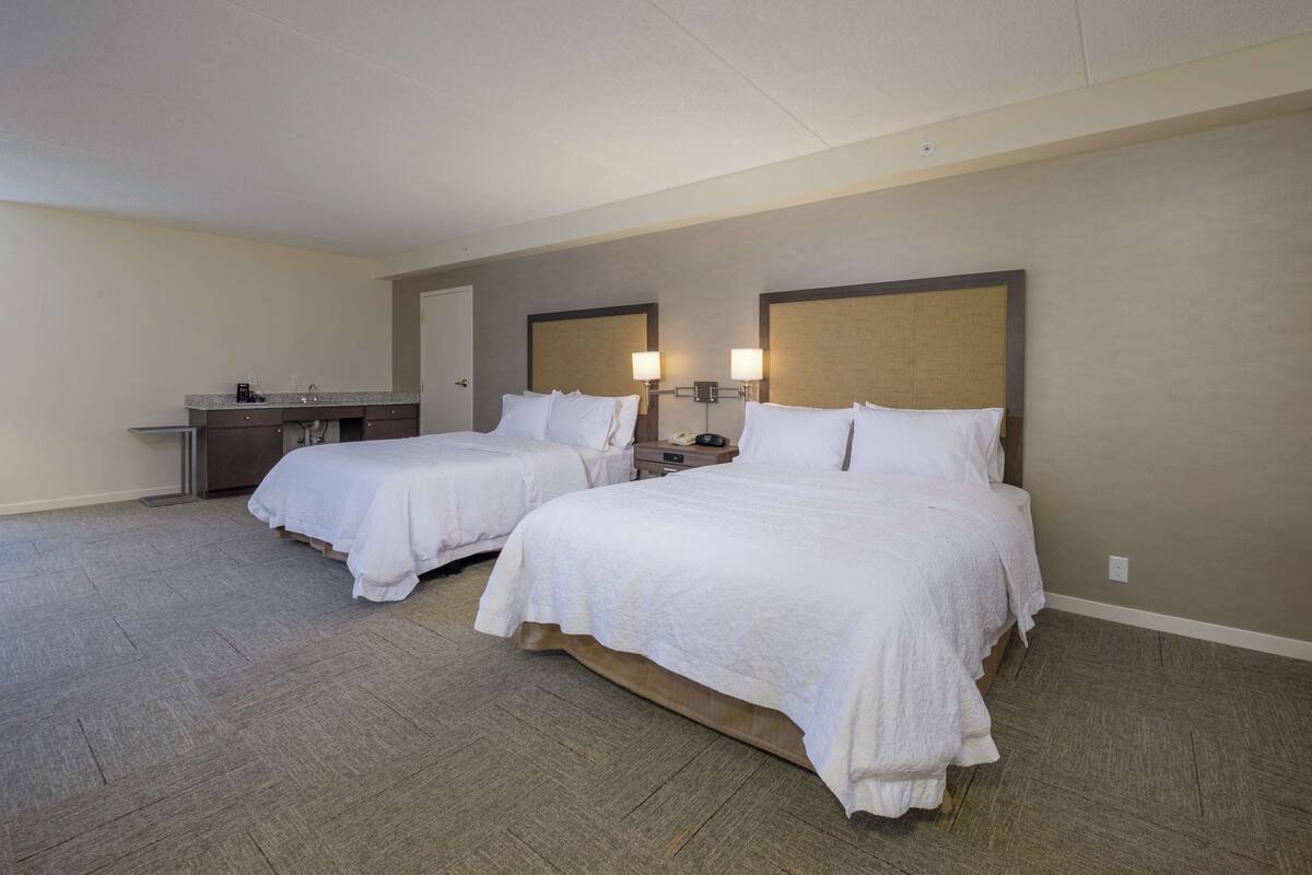 A hotel room with two beds, a desk, and a nightstand with lamps.
