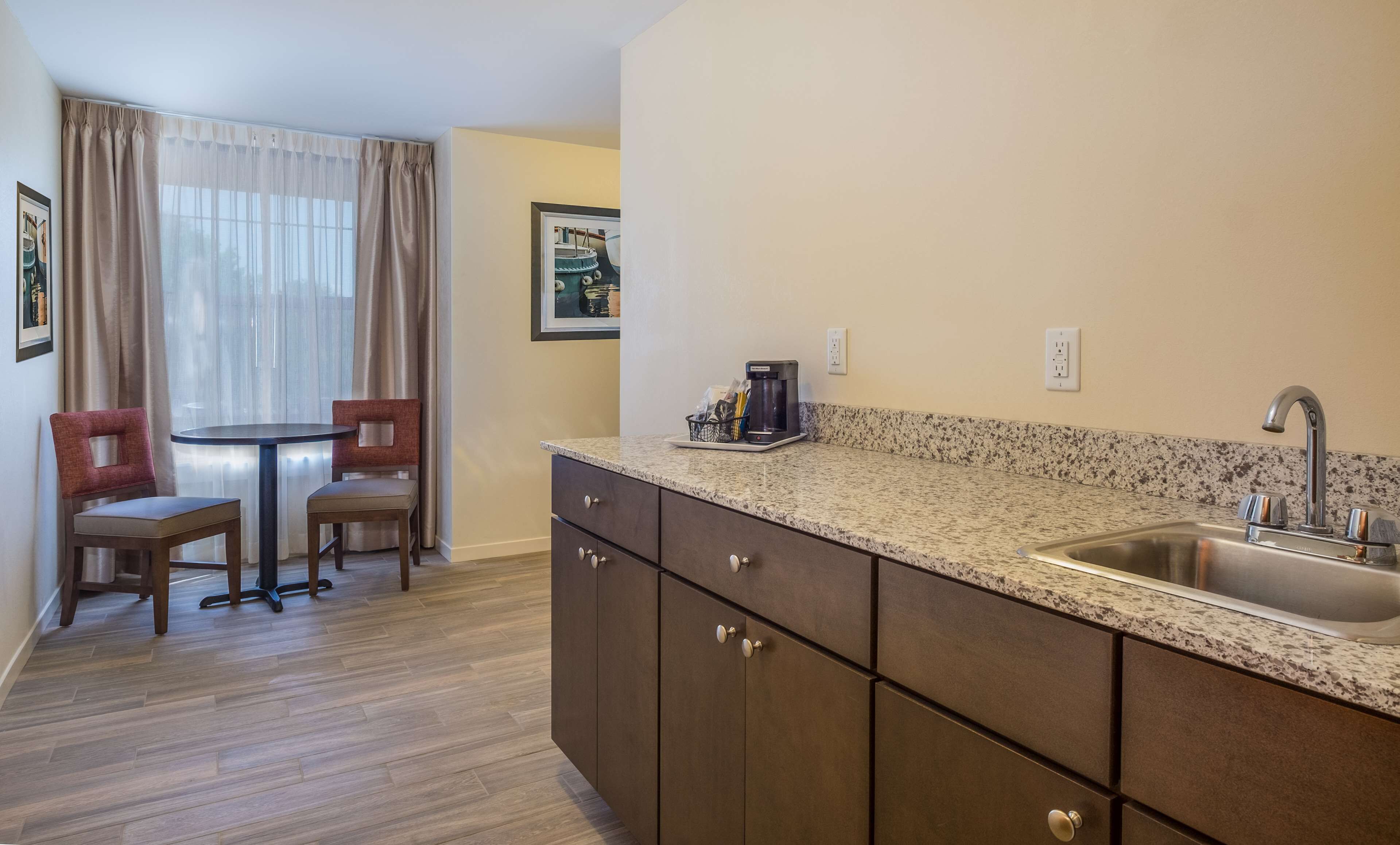 A compact kitchen with a granite countertop, a sink, and a coffee maker. There is a dining area with two chairs and a table.