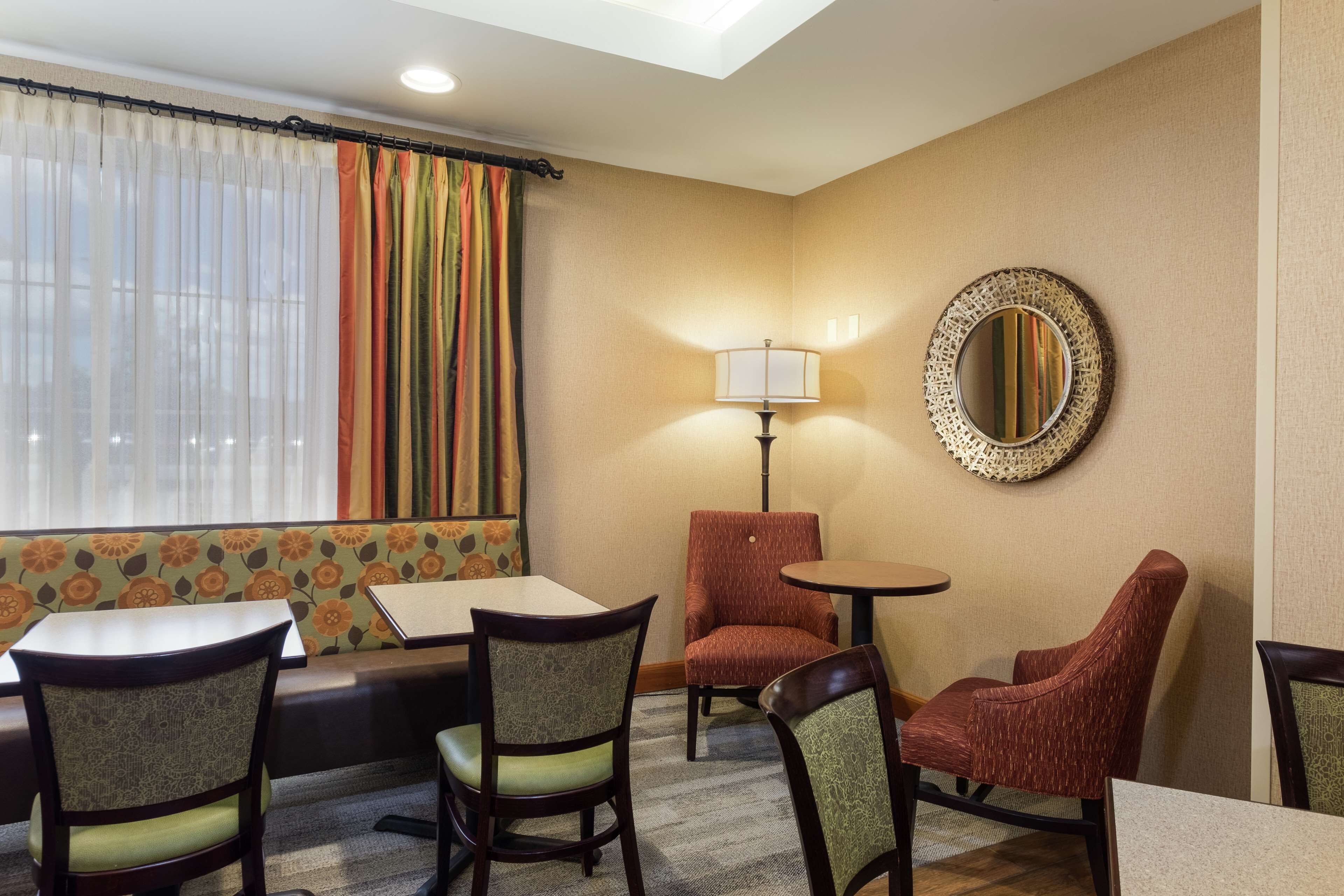 A hotel room with a seating area featuring a sofa, two armchairs, and a small table. A lamp and a mirror are on the wall.