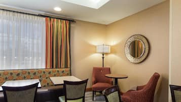 A hotel room with a seating area featuring a sofa, two armchairs, and a small table. A lamp and a mirror are on the wall.