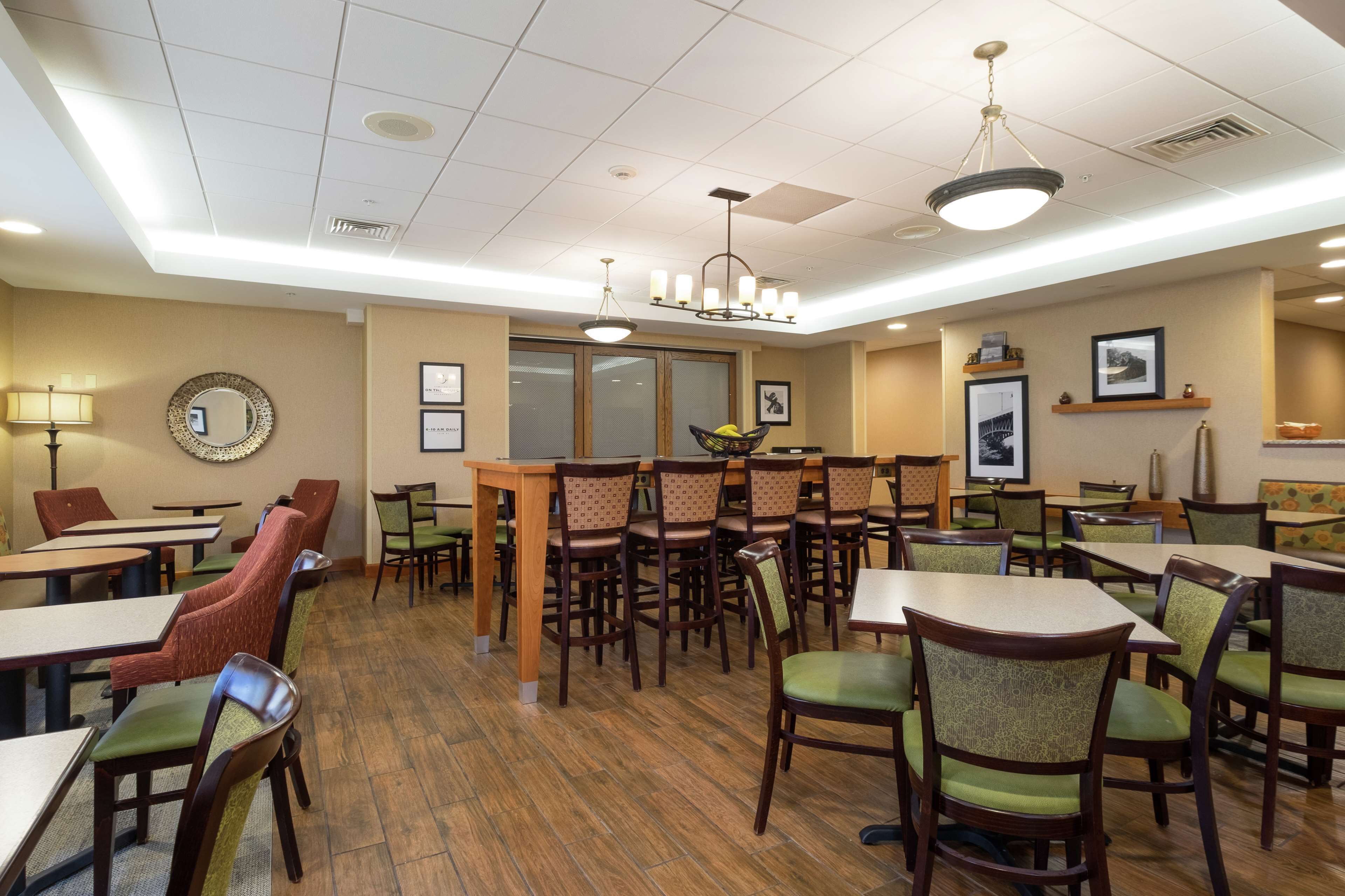 A dining area with multiple tables and chairs, a chandelier, framed pictures on the walls, and a window with blinds.