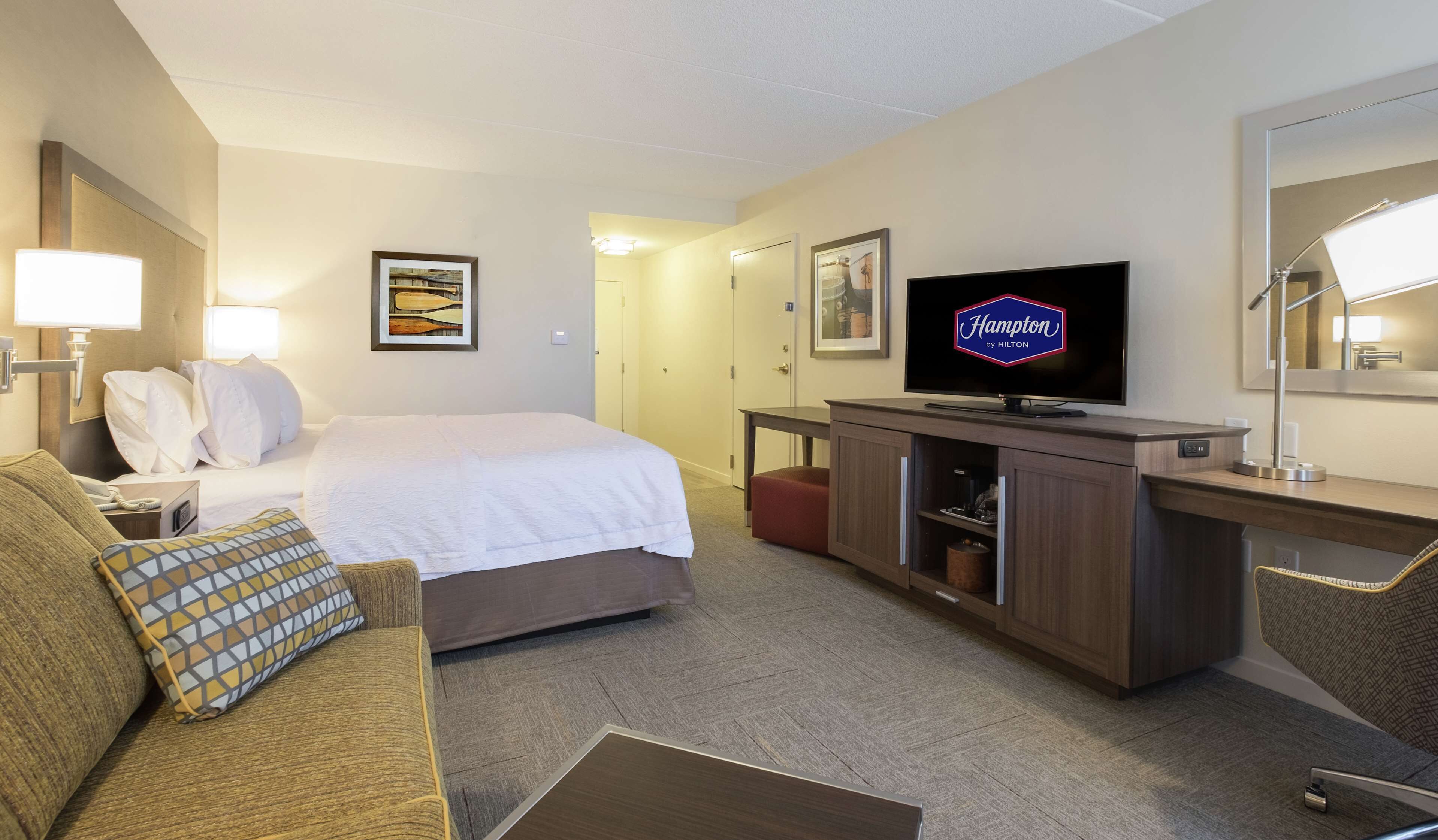 A hotel room with a bed, a desk, a television, and a mirror.