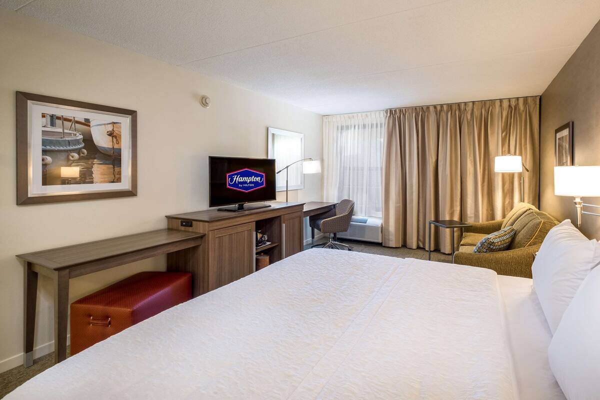 A hotel room with a bed, a desk, a chair, a television, and a window with curtains.