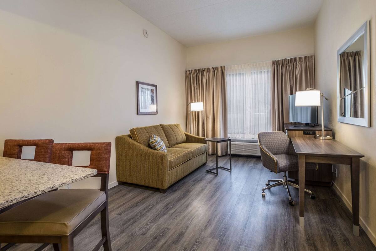 A hotel room with a bed, a sofa, a desk, a chair, a TV, and a window with curtains.