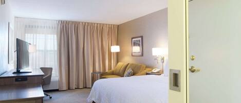 Una habitación de hotel con cama, escritorio, silla, televisor y puerta.
