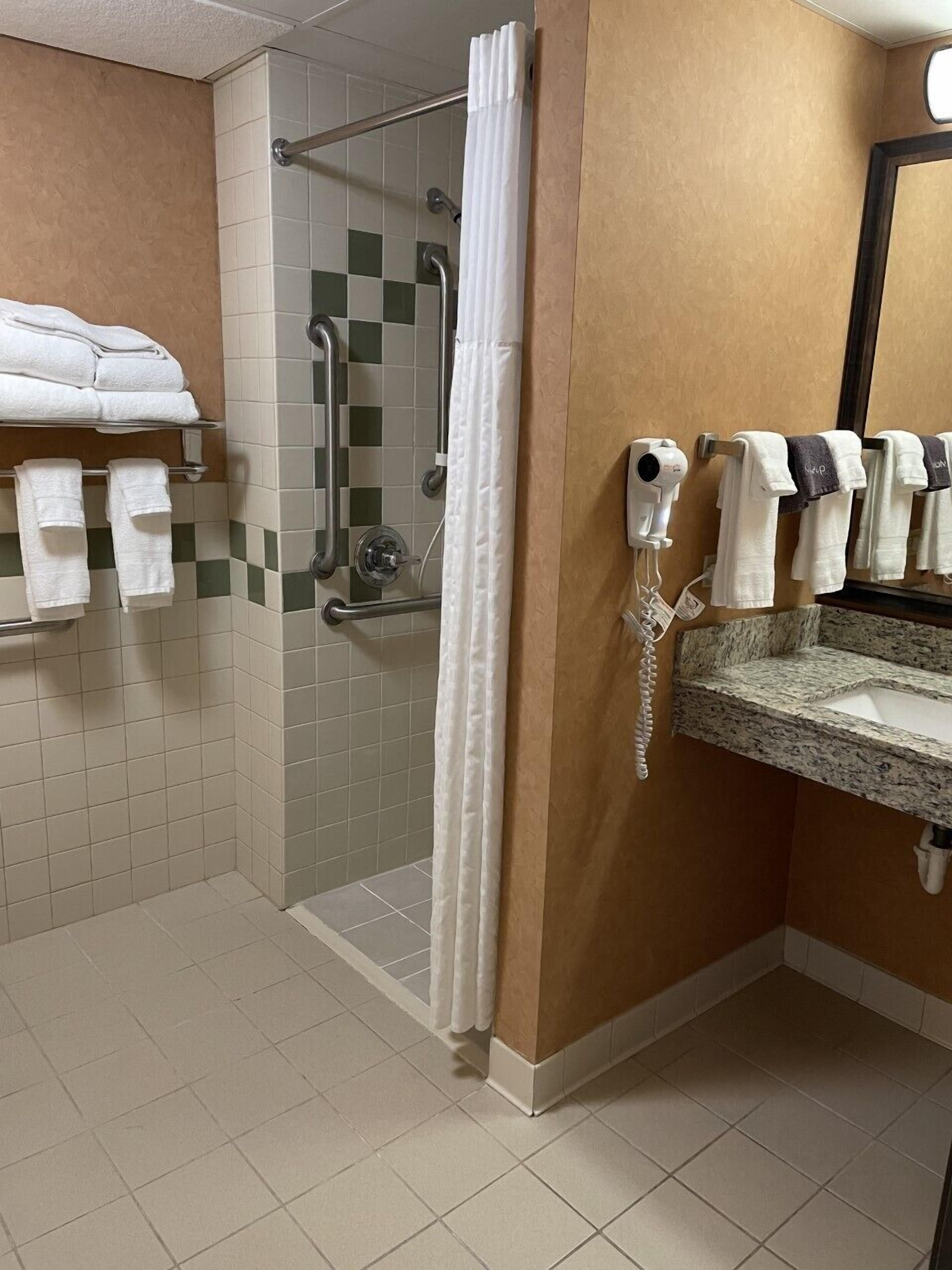 A hotel bathroom with a shower area, a vanity with a sink, and a towel rack with towels.