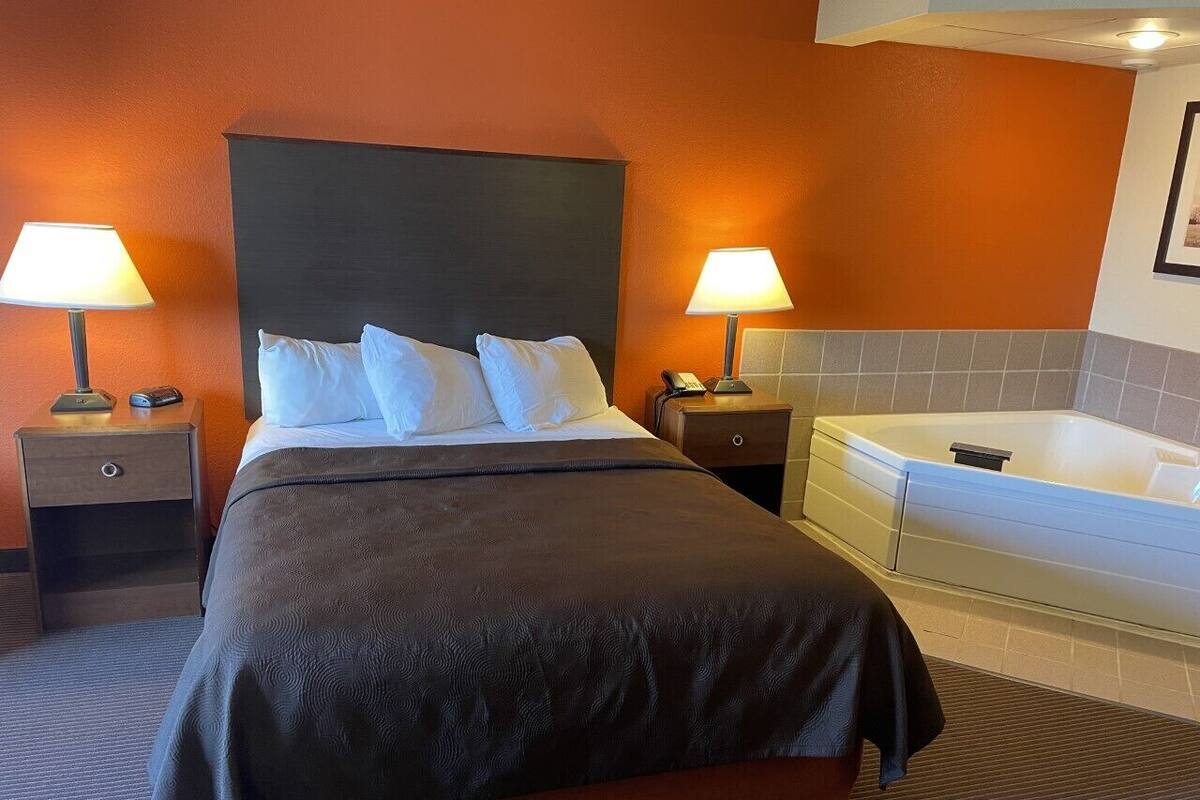 Habitación de hotel con una cama grande, dos mesitas de noche con lámparas, una bañera empotrada y un cuadro en la pared.