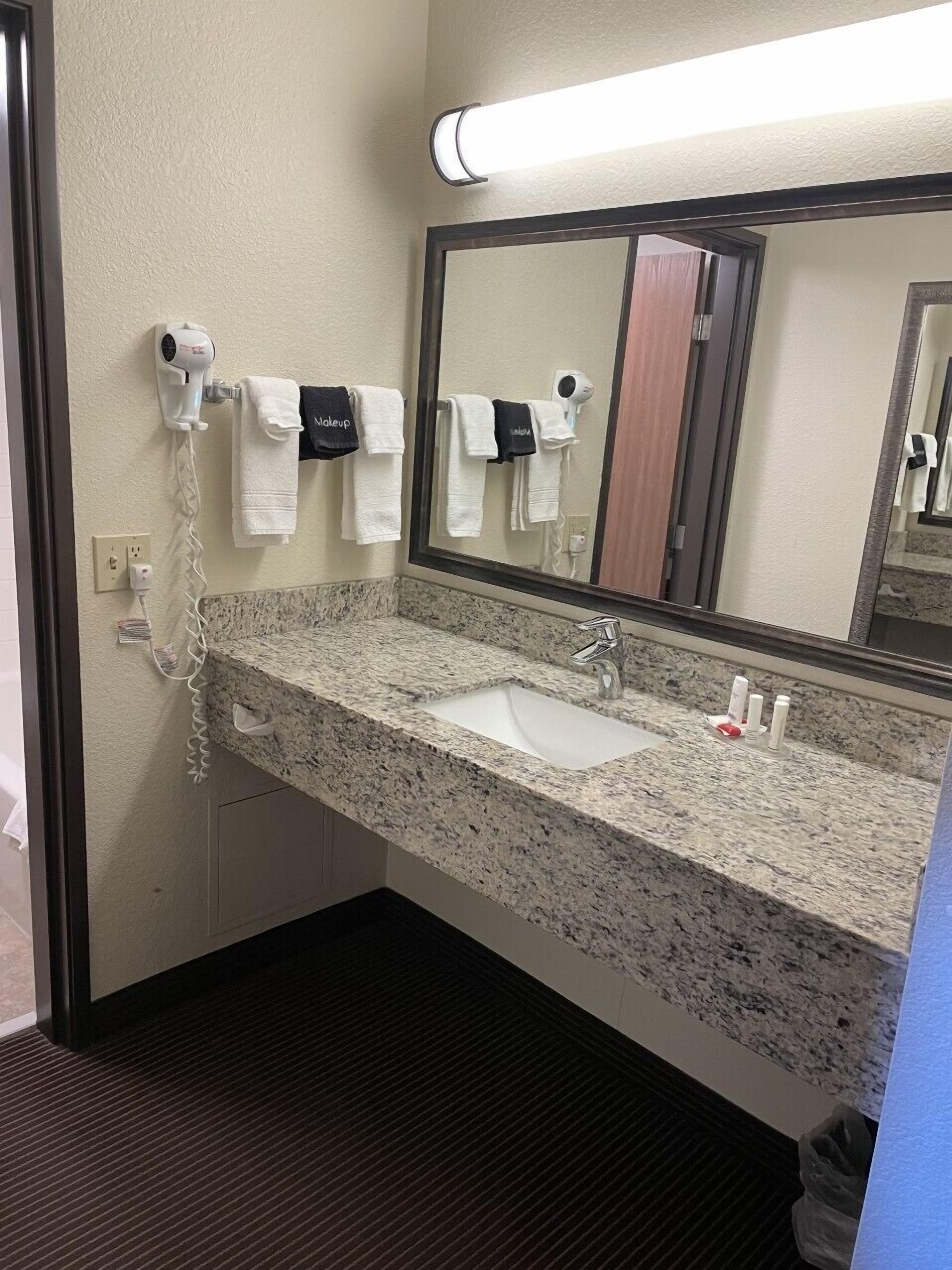 A bathroom with a granite countertop sink, a mirror, and a hairdryer on a wall-mounted rack.