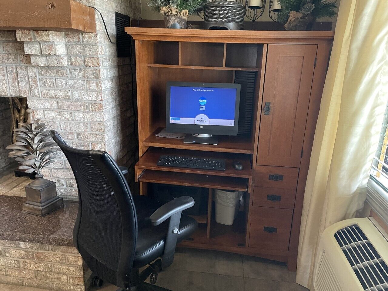 Un espacio de trabajo en casa con una computadora, silla y escritorio de madera frente a una pared de ladrillo.