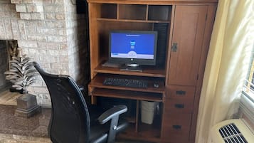 Un espacio de trabajo en casa con una computadora, silla y escritorio de madera frente a una pared de ladrillo.