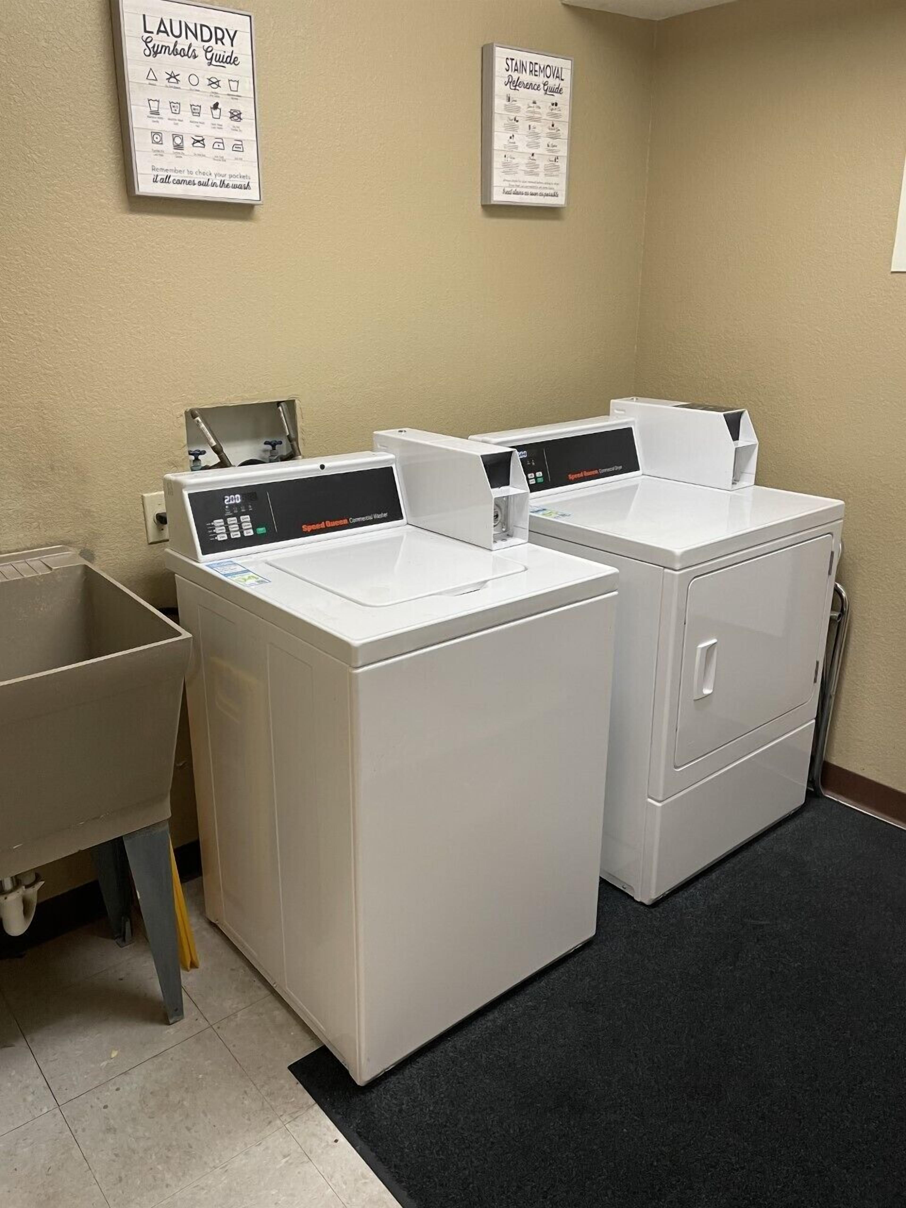 Une buanderie équipée de deux lave-linge à chargement frontal et d’un appareil combiné lave-linge et sèche-linge. Deux panneaux explicatifs illustrant les symboles de lavage sont accrochés au mur.