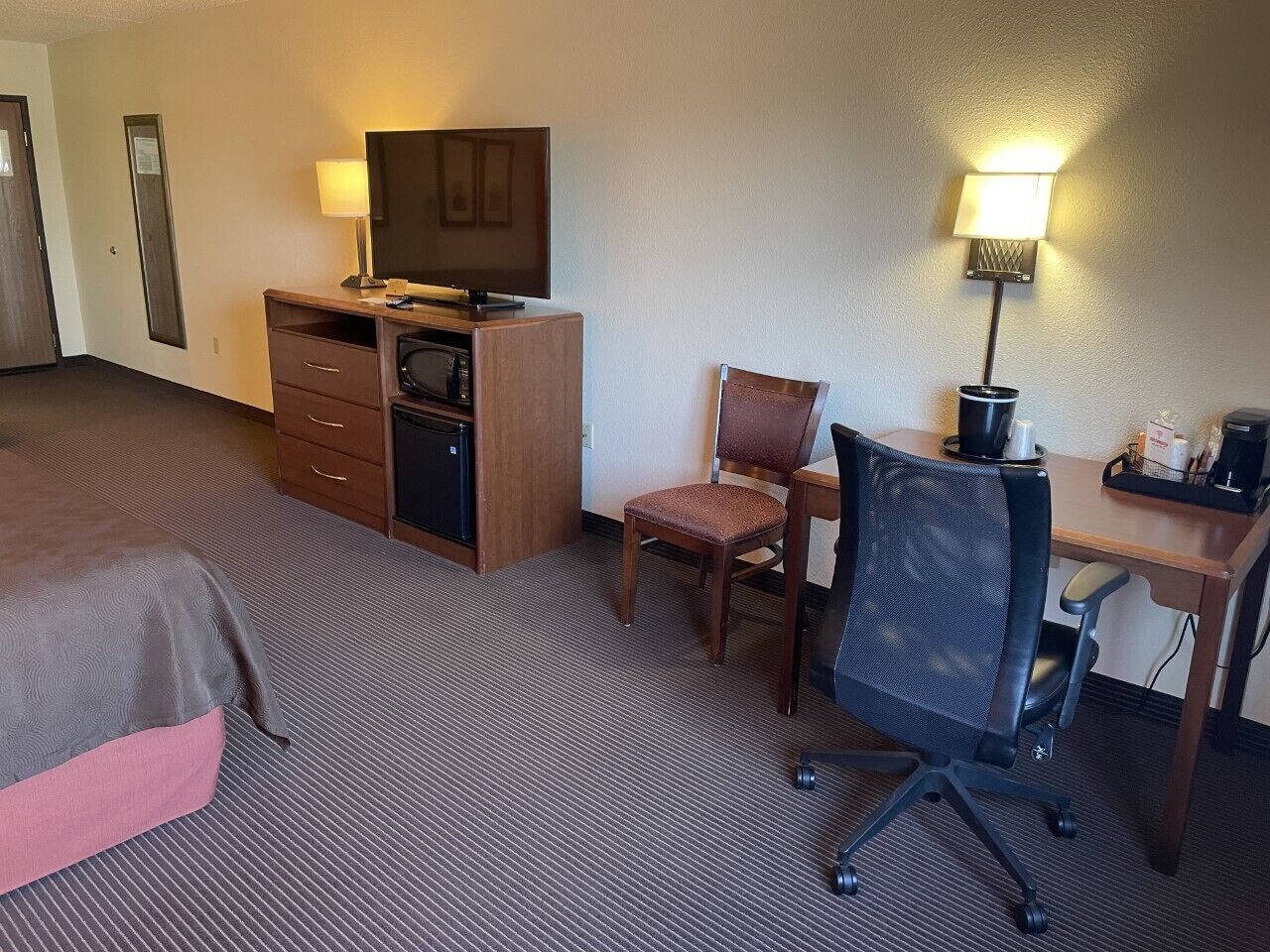 Habitación de hotel con cama, escritorio, silla, televisor, lámpara y microondas.